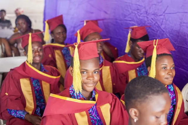A graduand smiling towards the camera among classmates in maroon caps and gowns at the graduation ceremony