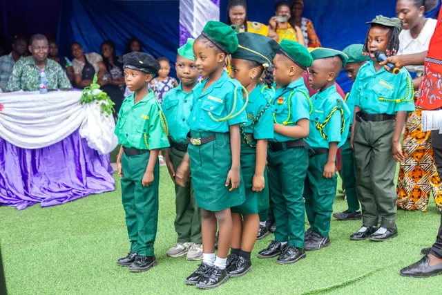 Preschool pupils in green ceremonial uniforms and berets lined up to perform at a school event