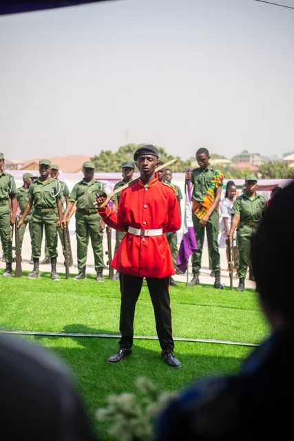 A pupil in a red ceremonial tunic leading the school parade on the field