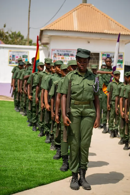 A line of pupils in green parade uniform marching in formation past the school building