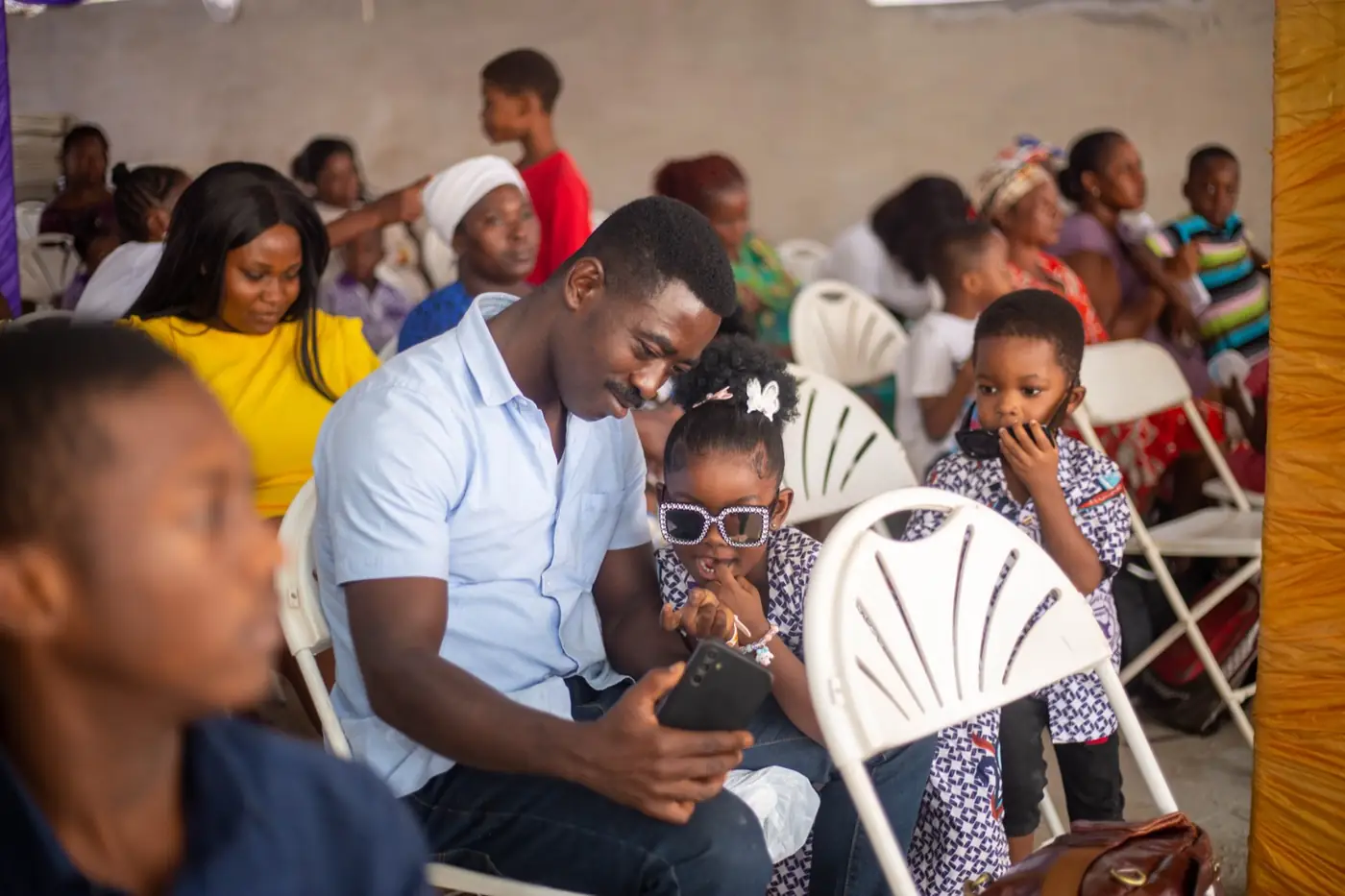 A parent and two young children seated among the audience at a school ceremony